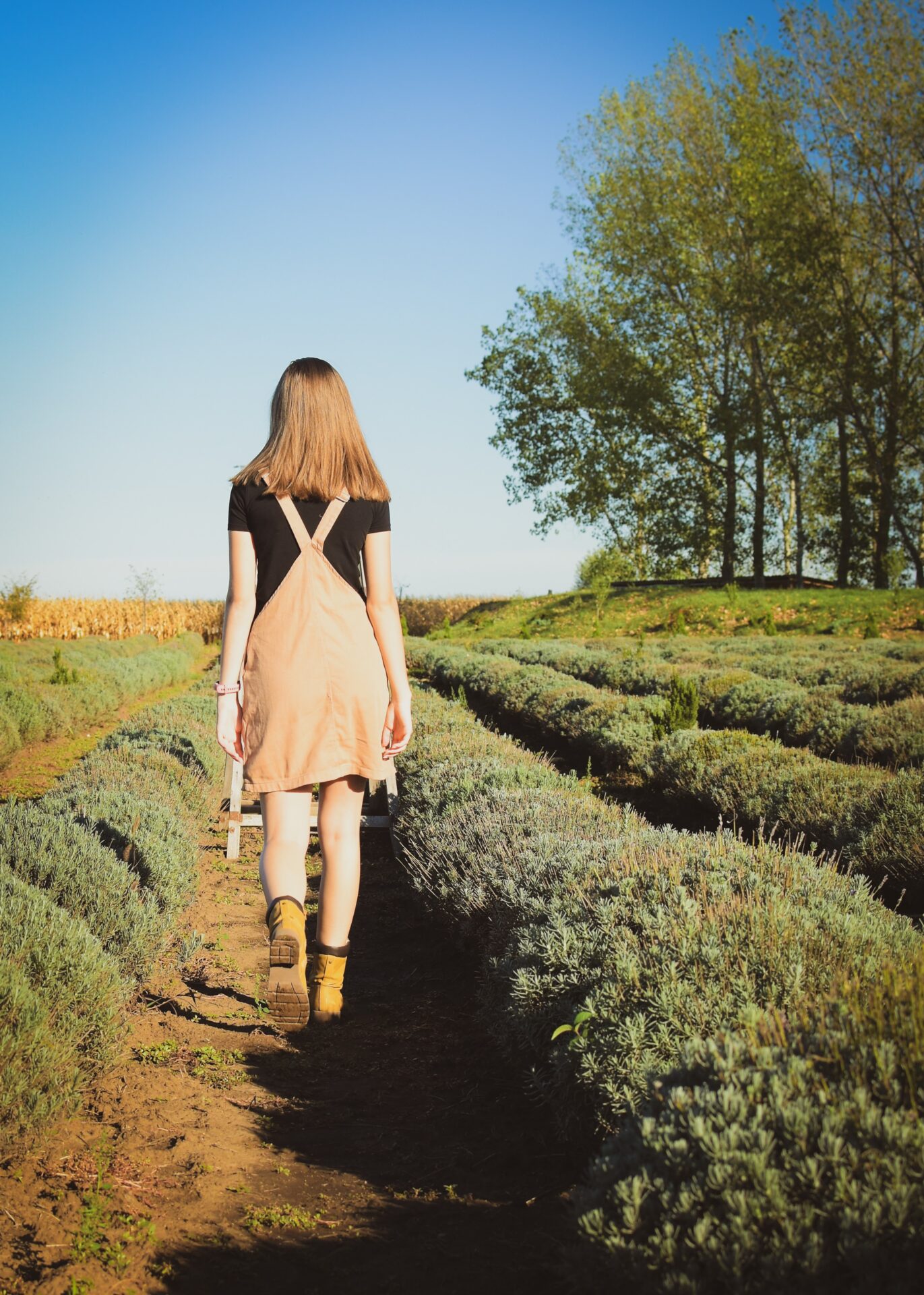 woman in beige sleeveless dress walking on pathway between green grass field during daytime